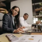 Dua profesional bekerja dengan laptop dan kalkulator di kantor modern